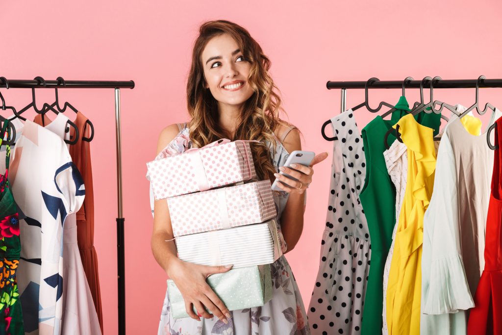 In this blog post, we’ll explore why engaging existing customers is critical to business success and how Telephonetics' Message On Hold solution can enhance the customer experience, build brand loyalty, and increase overall profitability. - Happy woman with shopping packages standing near clothing racks with cell phone out